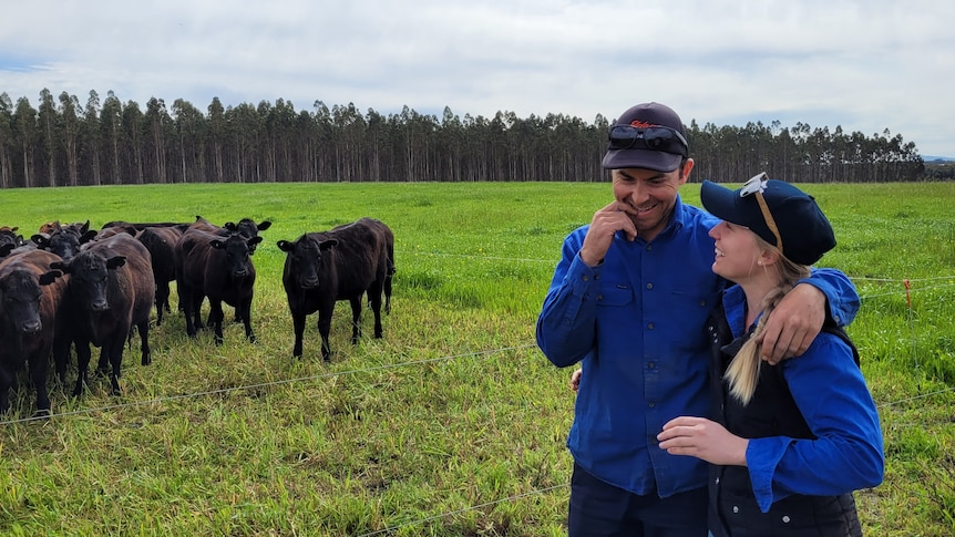 Jess and Cody Shilling stand on their pasture with some black cattle.