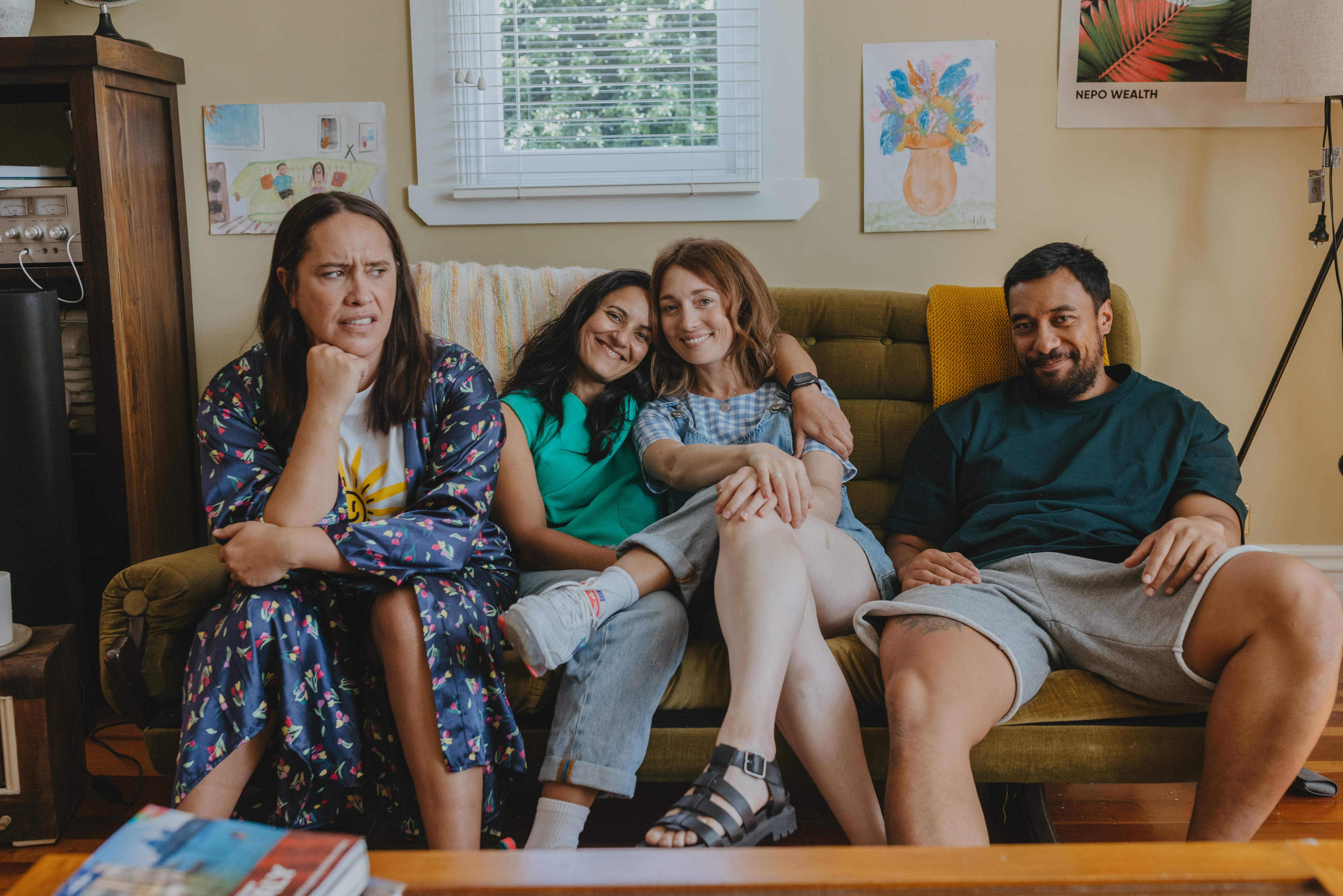 Four people sitting on a couch, two young women in the middle, smiling with their arms around each other.