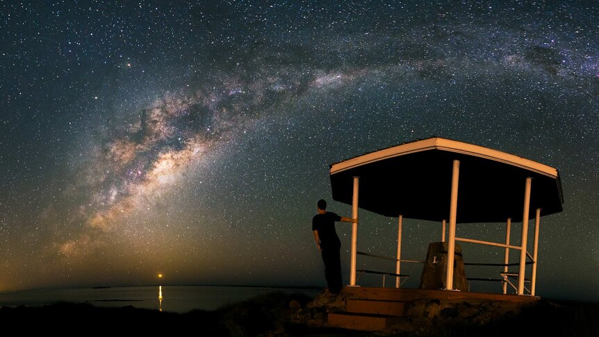 Man looks out over sea and starry night from lookout
