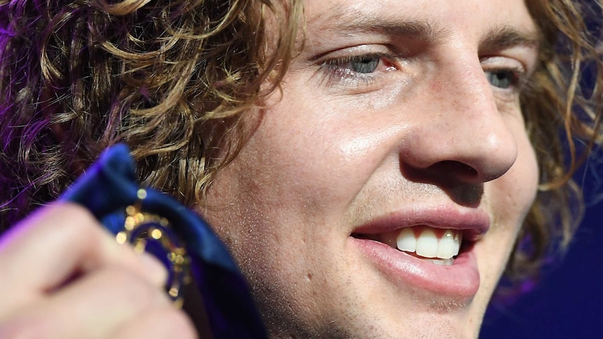 A tight head shot of Nat Fyfe holding up the Brownlow Medal near his face.
