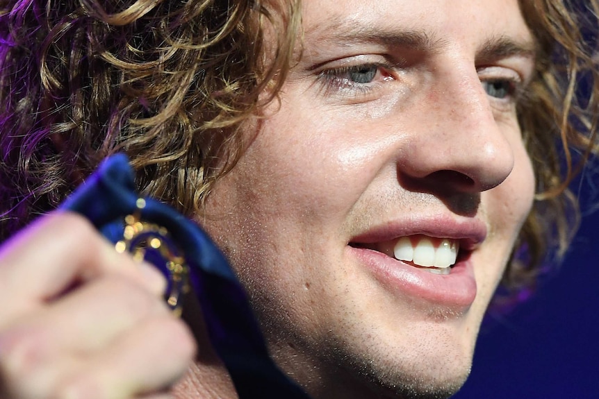 A tight head shot of Nat Fyfe holding up the Brownlow Medal near his face.