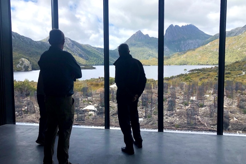 People look out a window at a lake and a mountain