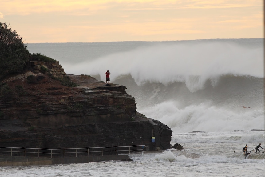 A man stands on the rocks photographing the swell at Narrabeen North beach.