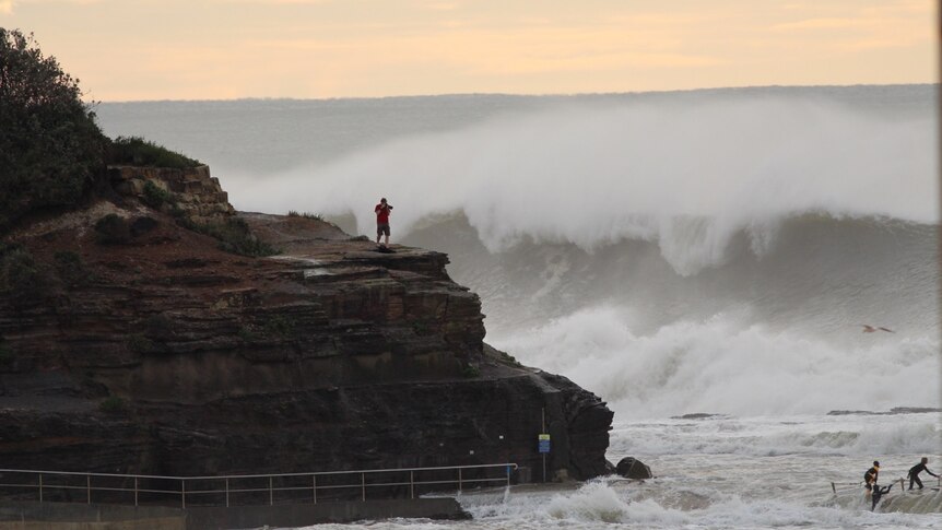 A man stands on the rocks photographing the swell at Narrabeen North beach.