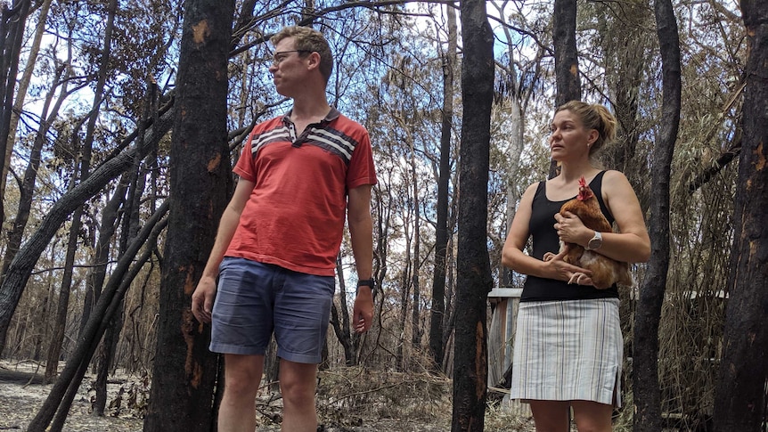 Andrew and Wendy O'Conner, Wendy holding a chicken, stand in burnt out bush on their propperty.