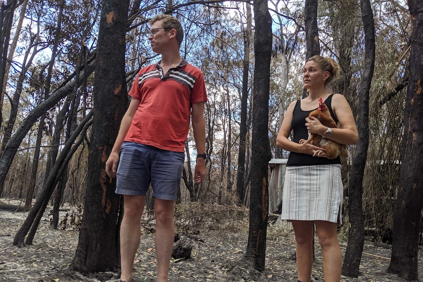 Andrew and Wendy O'Conner, Wendy holding a chicken, stand in burnt out bush on their propperty.