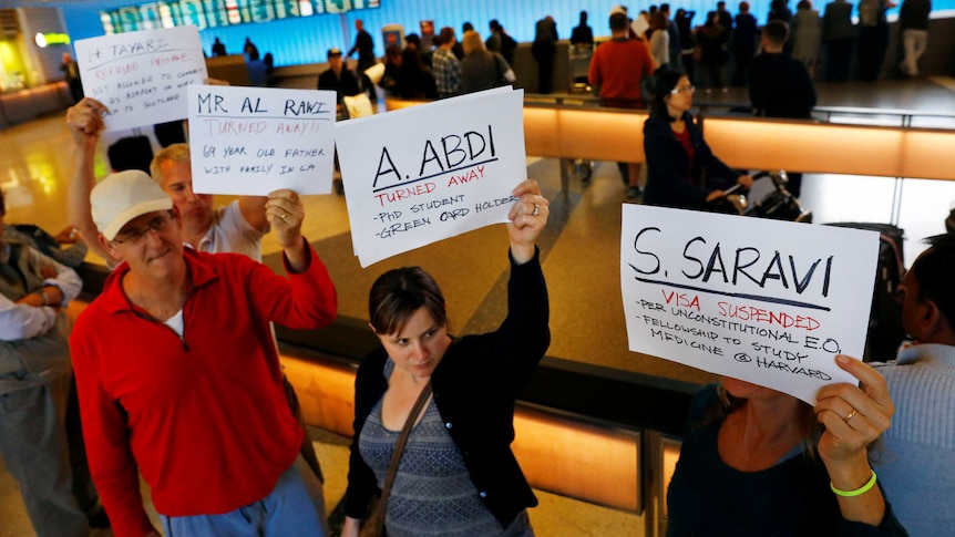 People hold signs with the names of people detained and denied entry at LAX