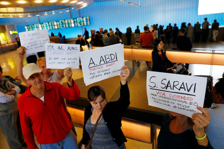 People hold signs with the names of people detained and denied entry at LAX