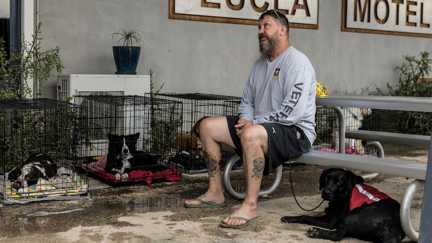 A man sitting down holding his dog on a lead.  