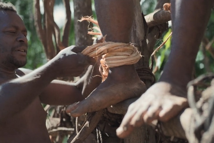 A man ties rope around another's ankle in preparation for taking a nagol jump.