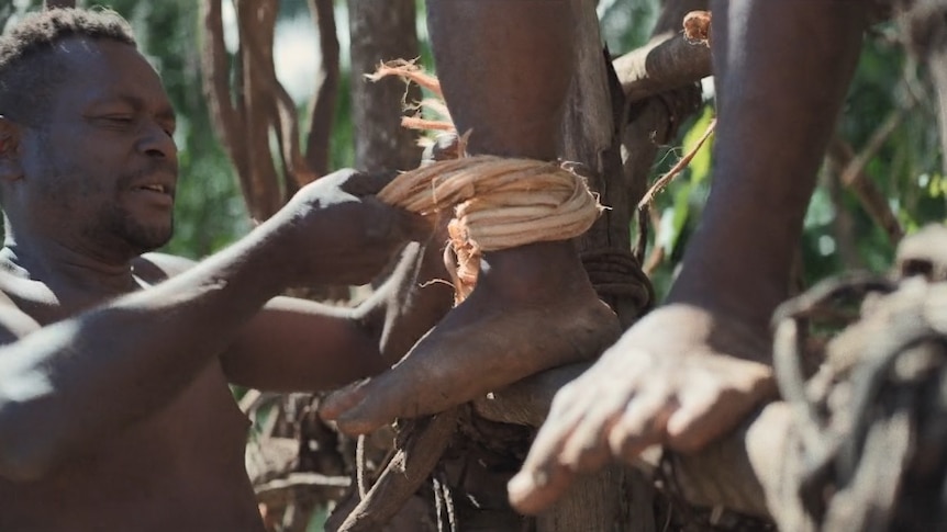 A man ties rope around another's ankle in preparation for taking a nagol jump.
