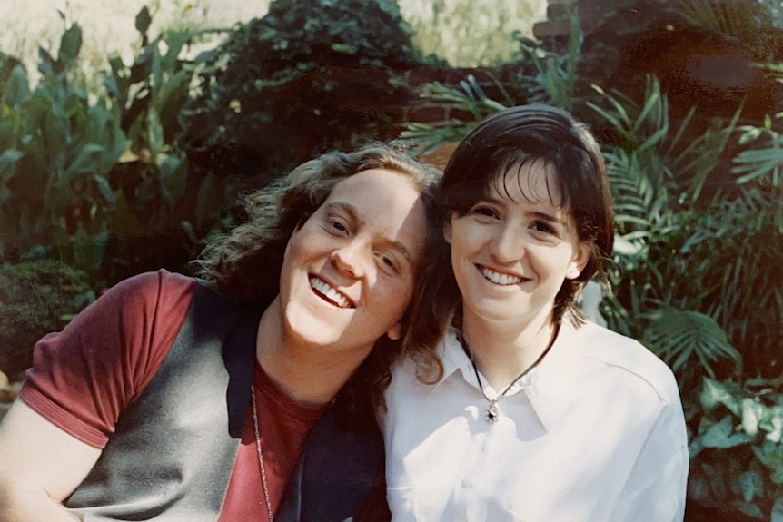 A young man leans his head on the shoulder of a young woman and smiles.