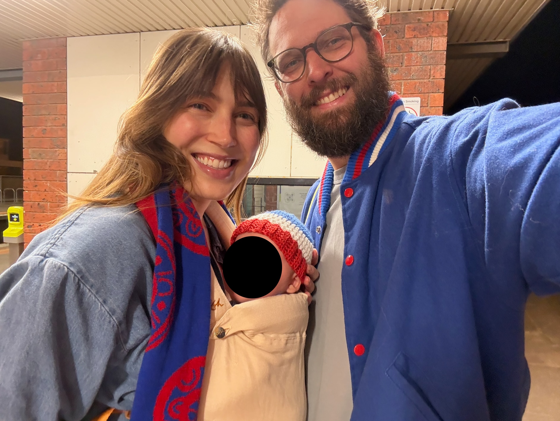 A smiling couple with a small baby in a carrier