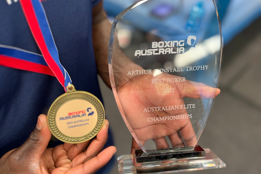 A close-up of a glass trophy and gold medal being held 