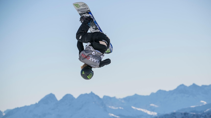 Tess Coady performs a trick on a snowboard with mountains in the background