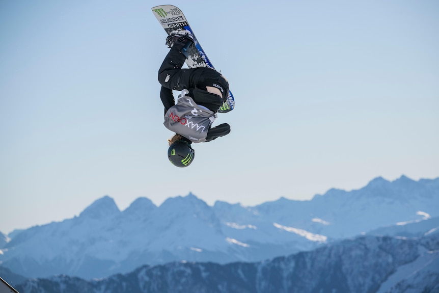 Tess Coady performs a trick on a snowboard with mountains in the background