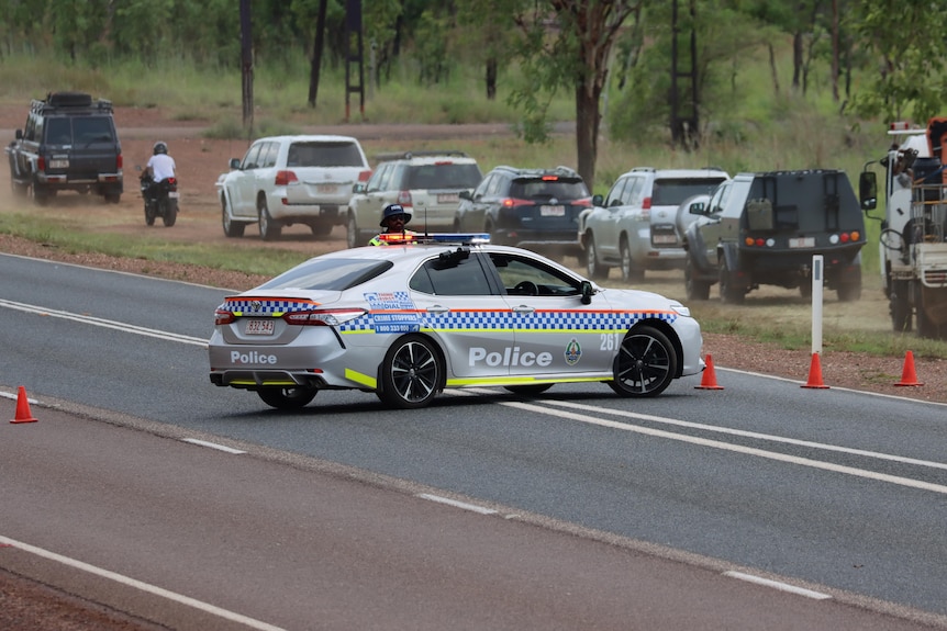 A police car parked across two lanes of the road, with vehicles needing to drive off-road behind it