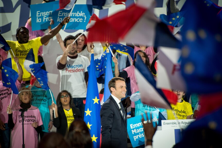 A man in a suit is swamped by supporters waving the French and European Union flags, wearing shirts that read Ensemble La France