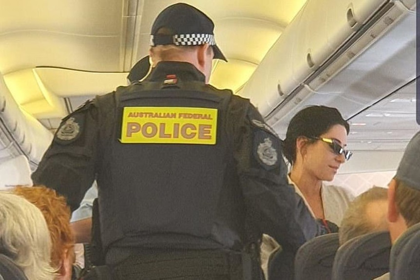 A police officer stands in the aisle of a packed flight.