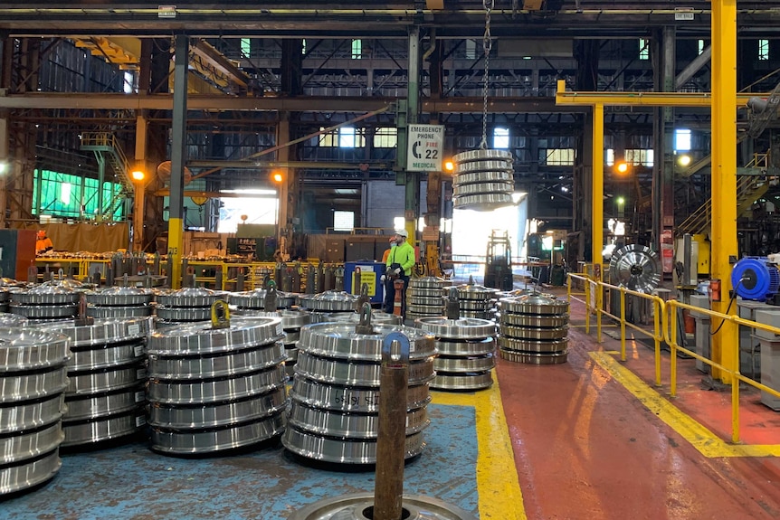 Molycop steel works factory floor with stacks of steel train wheels and a worker.