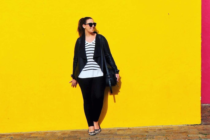Jayne Gorman of Girl Tweets World leans against a yellow wall in Cape Town for a story about packing luggage tips.