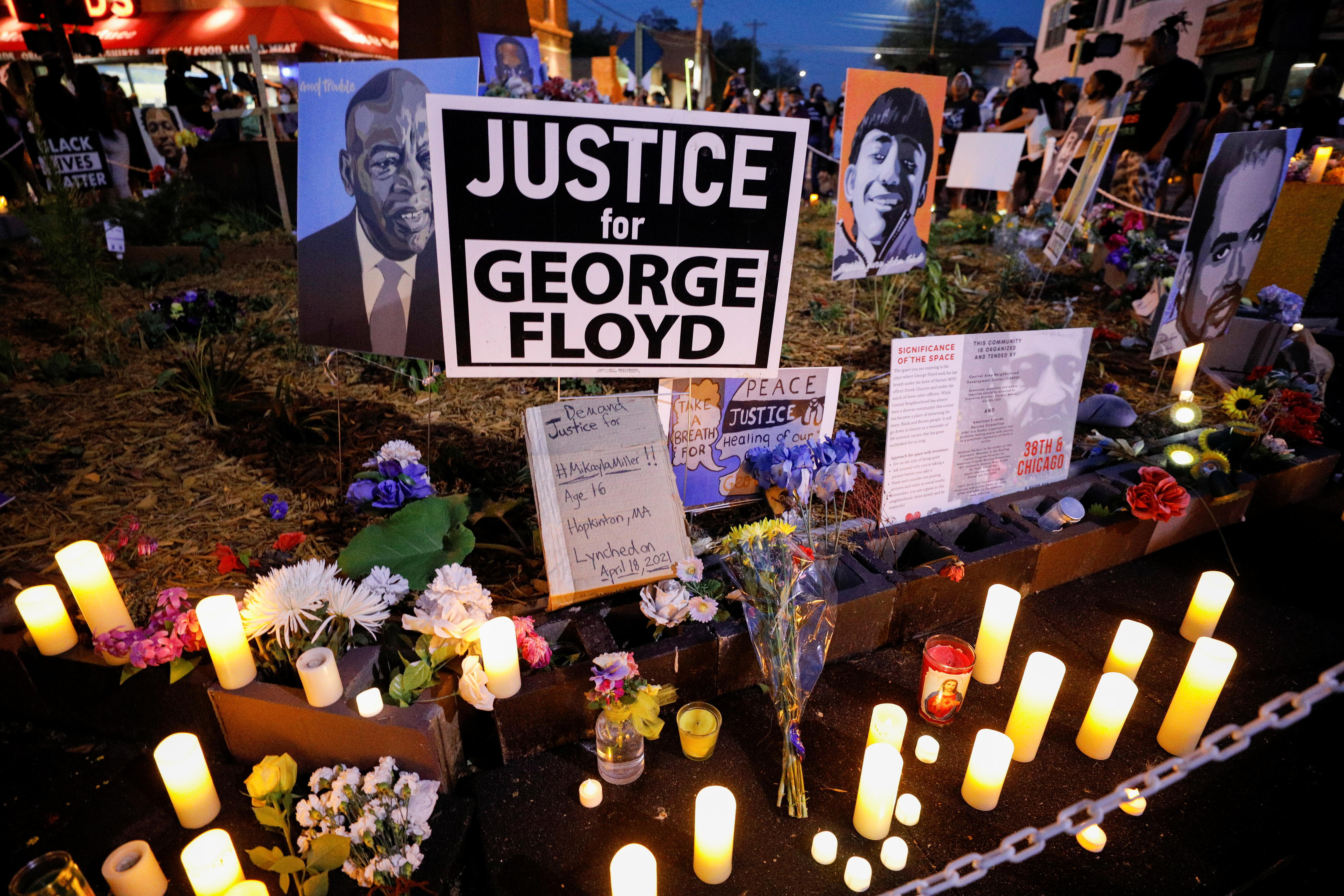Electric and LED candles and flowers are played on the ground next to a Justice for George Floyd sign.