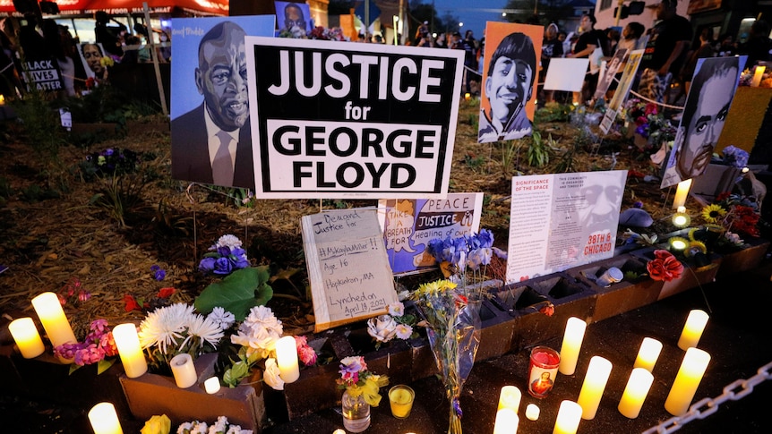 Electric and LED candles and flowers are played on the ground next to a Justice for George Floyd sign.