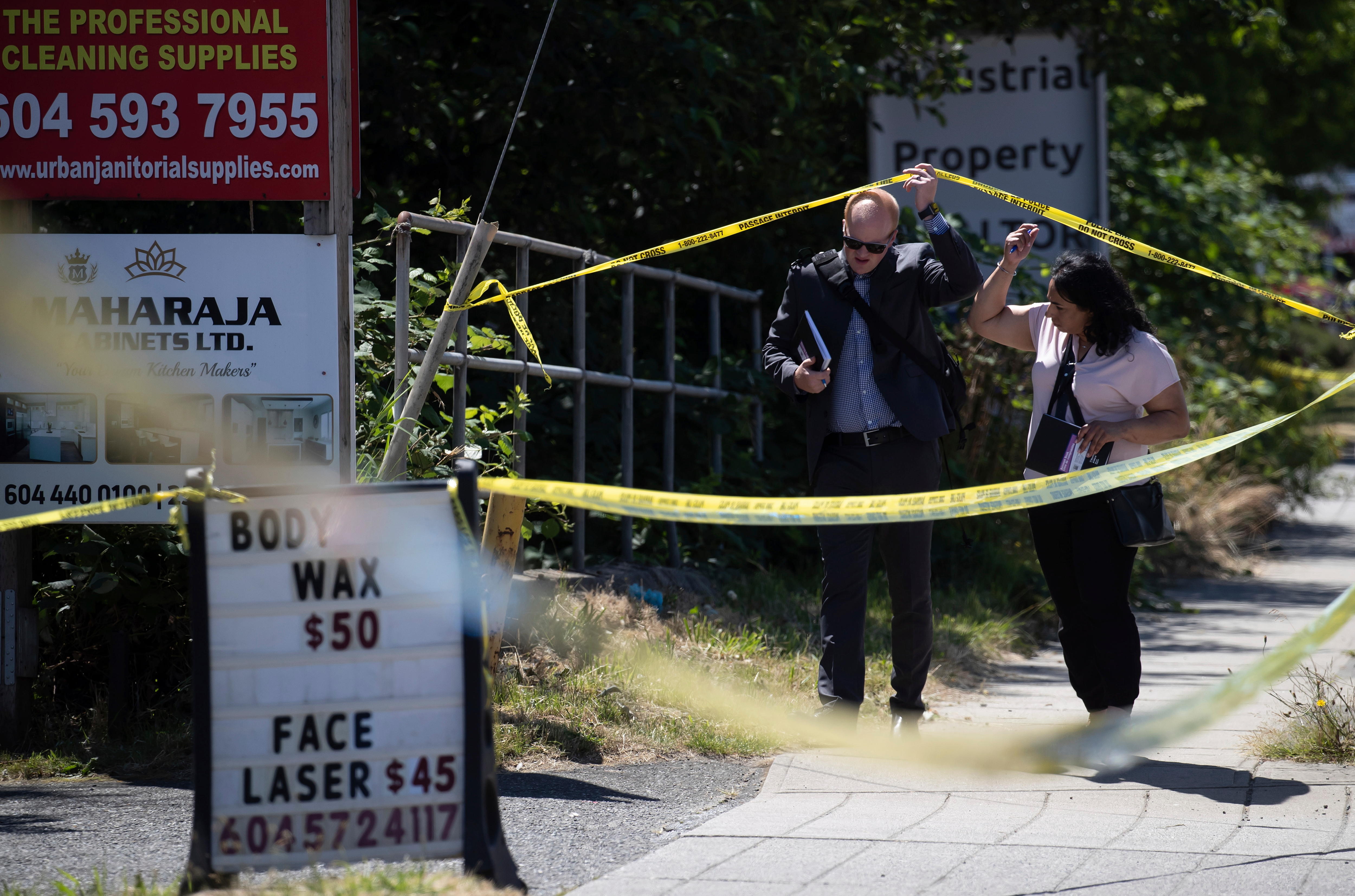 A male and female police officer duck under yellow police tape across a footpath at a crime scene. 
