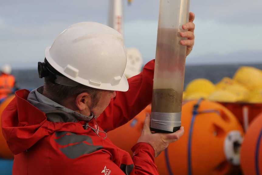 Craig Woodward examines the sediment from the sample, on board RV Investigator.