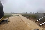 A picture of flood water flowing across a field, next to a building.