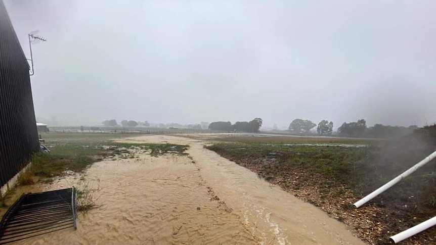 A picture of flood water flowing across a field, next to a building.