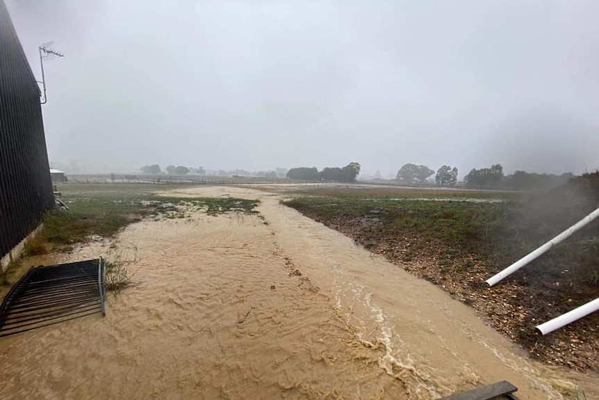 A picture of flood water flowing across a field, next to a building.
