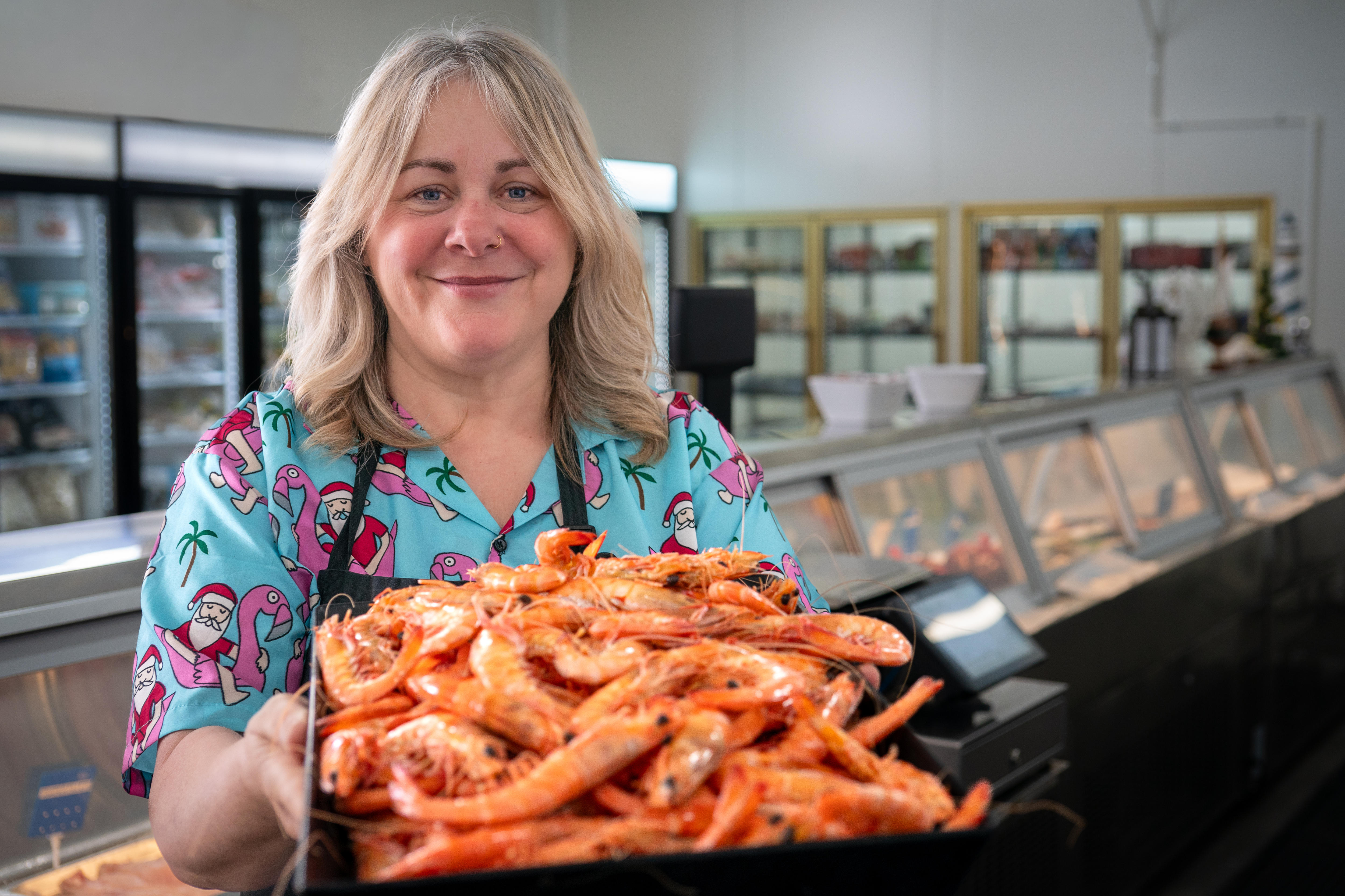 Uma mulher sorri para a câmera segurando uma bandeja com camarões inteiros cozidos