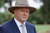 Anthony Albanese in an Akubra hat and jacket and tie stands in a park