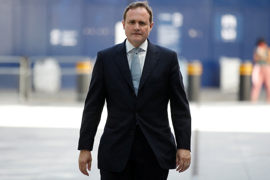 Man in suit with serious expression walks directly forwards