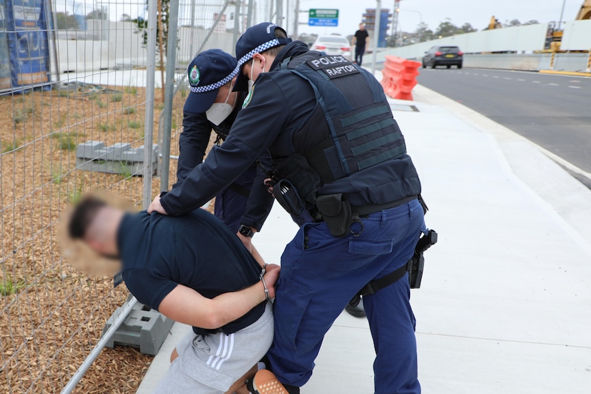 two police officers handcuffing a man against the fence