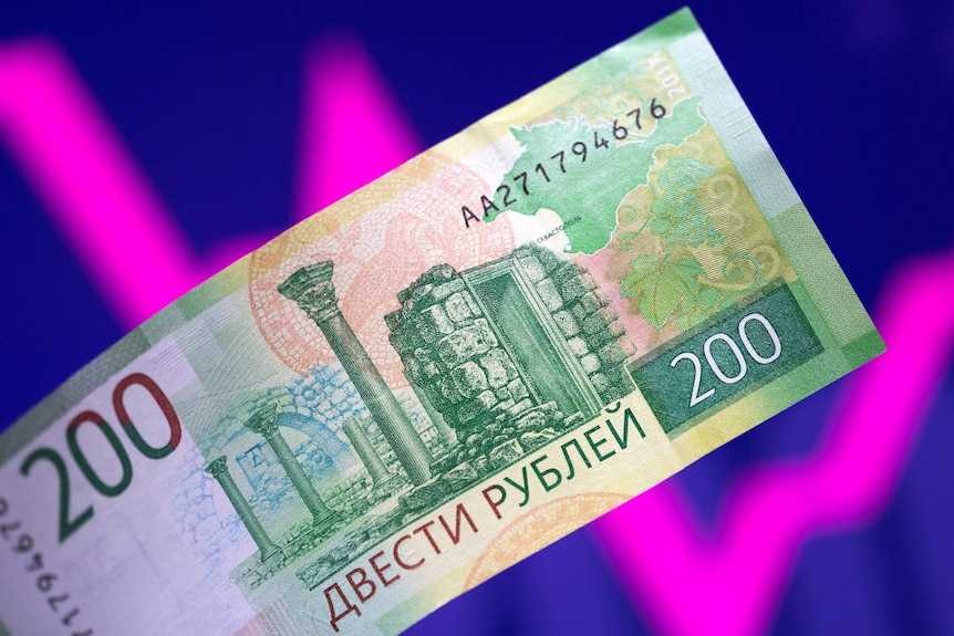 Illustration shows a Russian rouble banknote and a descending and rising stock graph.