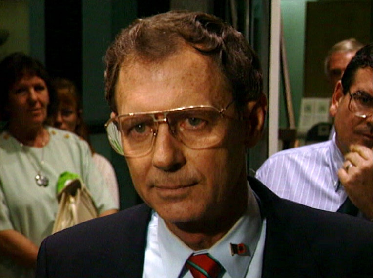 A headshot of a man wearing glasses and a suit.