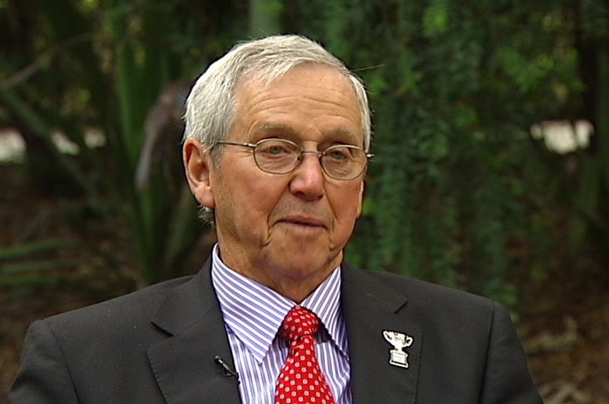 A man wearing glasses and a suit and tie sits looking at the camera