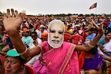 A woman wearing a mask of Prime Minister Narendra Modi dances as she attends an election campaign rally.