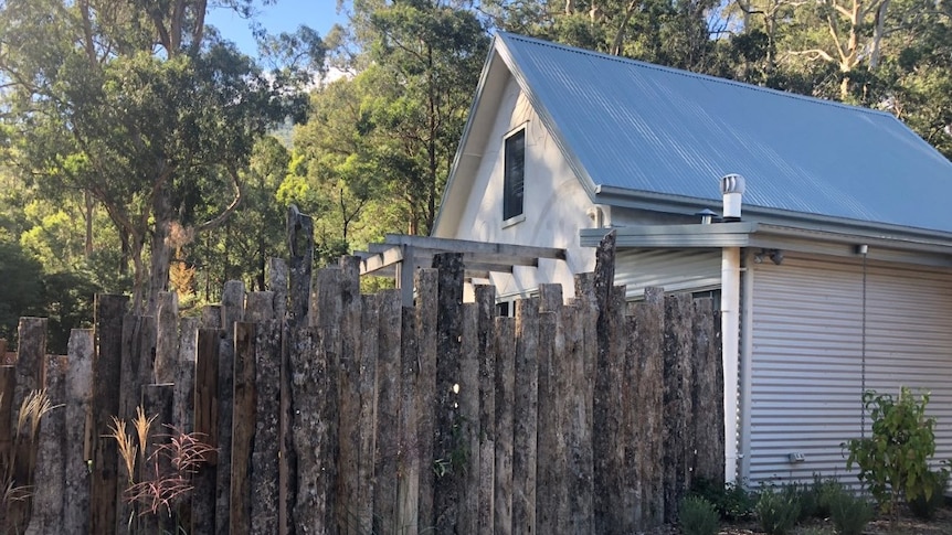 A house behind a wooden fence with trees around it.