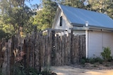 A house behind a wooden fence with trees around it.