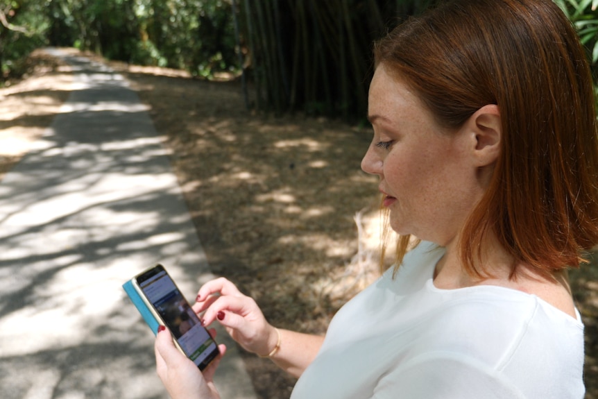 A woman looks at her phone at real estate listings.