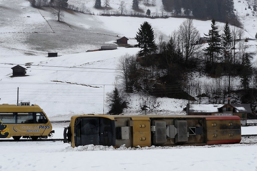 A train carriage lies on its side in the snow.