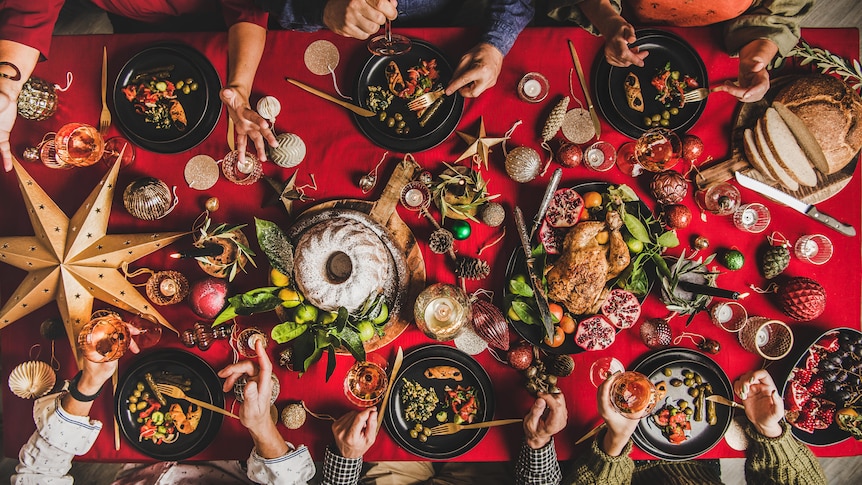 A birdseye view of a red-clothed table, plates of food and arms of guests.