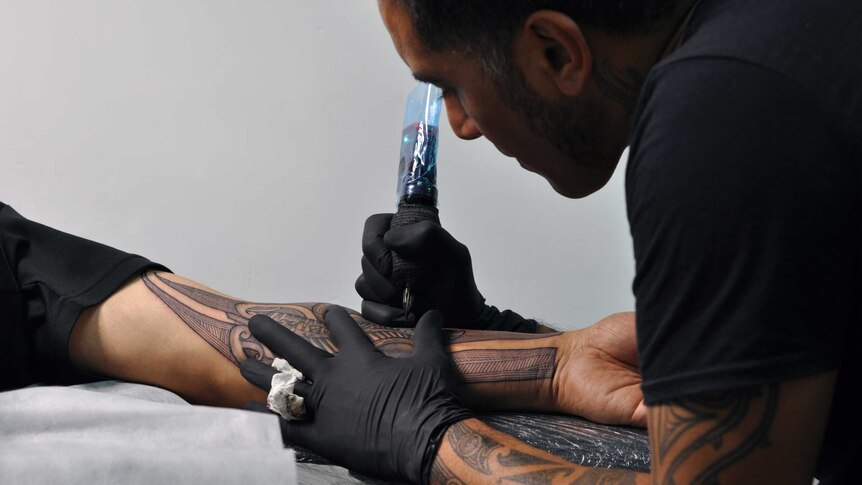 A Maori man focuses as he tattoos a traditional Moko design onto the arm of a man.