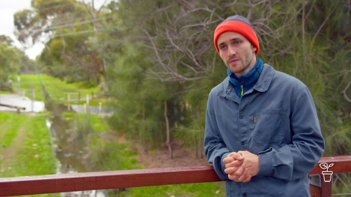 Man wearing a red beanie standing on a bridge over a stream