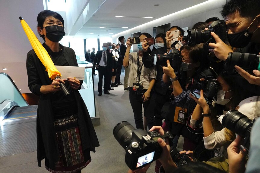 A woman in Hong Kong holds up a resignation letter while clasping a yellow umbrella as she stands in front of a media pack.