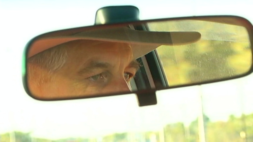 Reflection of a man wearing a hat in a car rearview mirror