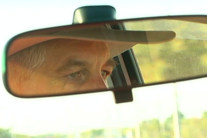 Reflection of a man wearing a hat in a car rearview mirror